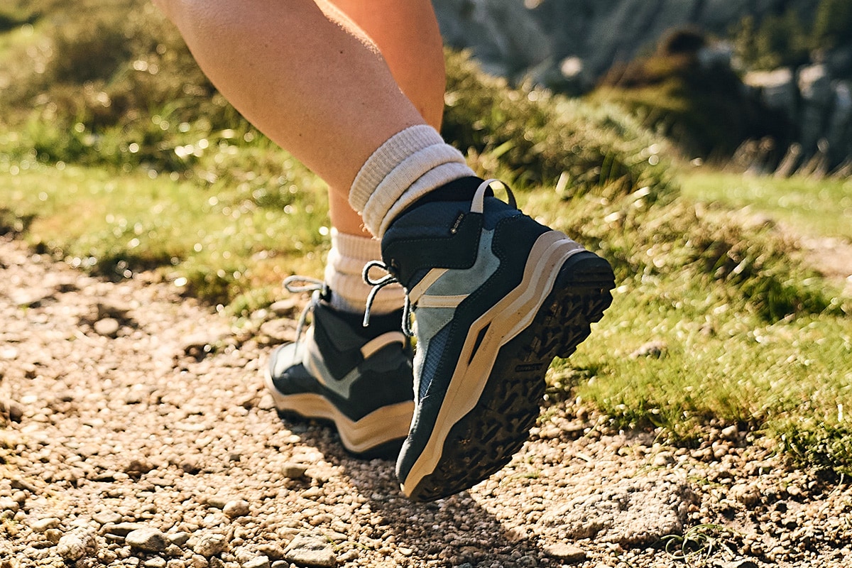 Hiker in blue hiking boots on a rocky path with green grass in the background.